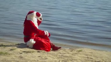 Noel Baba bir çanta dolusu hediyeyle nehir ya da göl kenarında oturur. Noel Baba suyun içine bakar.