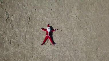 Noel Baba kumlu sahilde yatar ve sakalını okşar, gözlüklerini düzeltir. Üst görünüm