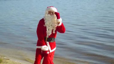 Noel Baba bir çanta dolusu hediyeyle nehir ya da göl kıyısında durur.