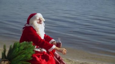 Noel Baba bir gölün kumlu sahilinde bir çanta dolusu hediyeyle oturur ve bir sigara içer ve şişeden alkol içer. Sarhoş Noel Baba..