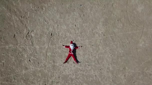 Święty Mikołaj leży na piaszczystej plaży. Widok góry. Kamera przesuwa się w lewo. Mikołaj w tropikach — Wideo stockowe