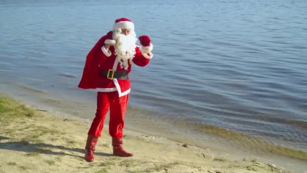 Санта Клаус стоит у океана или озера с мешком подарков — стоковое видео