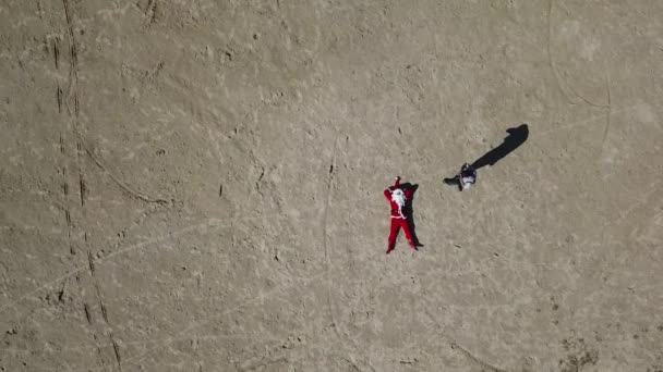 Babbo Natale è sdraiato sulla spiaggia sabbiosa Babbo Natale è avvicinato da un fotografo e scatta foto. Vista dall'alto. La telecamera si allontana verso l'alto. Babbo Natale ai tropici — Video Stock