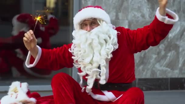 Santa sitter nära stadens kontor byggnad och håller tomtebloss — Stockvideo