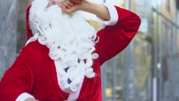 Slechte dronken Kerstman zit in de buurt van een stadskantoor. De kerstman drinkt alcohol uit een fles op straat. — Stockvideo