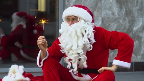 Papai Noel senta-se perto de edifício de escritórios da cidade e detém sparklers — Vídeo de Stock