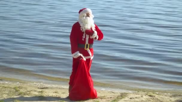 Kerstman staat bij de rivier of het meer met een zak cadeautjes — Stockvideo