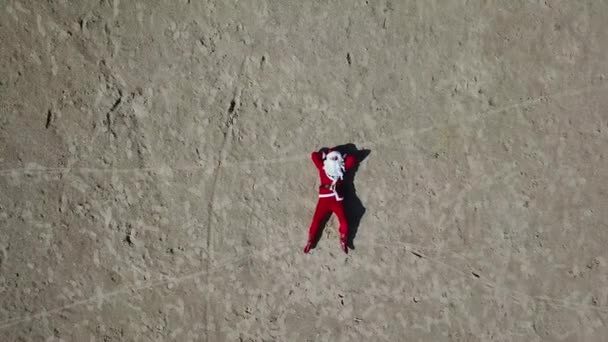 Bad Santa Claus est allongé sur une plage de sable et montre des gestes obscènes de la main. Père Noël relaxant. Vue du dessus — Video