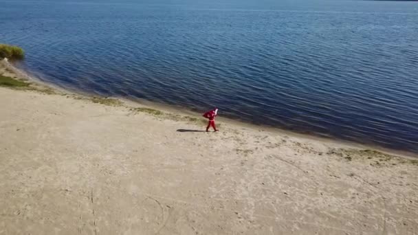 Cansado Santa Claus va con una bolsa de regalos a lo largo de la orilla del lago. Vista superior — Vídeos de Stock