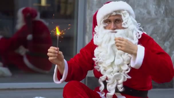 Santa Claus se sienta cerca del edificio de oficinas de la ciudad y tiene chispas — Vídeos de Stock