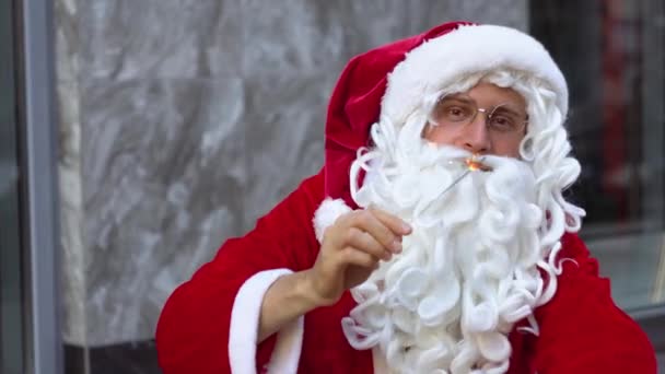 Santa sitzt in der Nähe des städtischen Bürogebäudes und hält Wunderkerzen in der Hand — Stockvideo