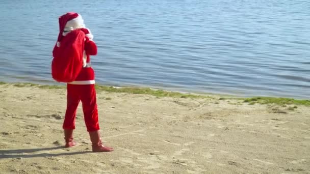 Papai Noel carrega um saco de presente ao longo do mar ou lago — Vídeo de Stock