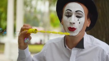 Eğlenceli pandomimci dışarıda sabun köpüğü üflüyor.