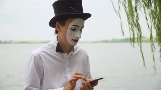 Mime divertido senta-se junto ao lago com um telefone — Vídeo de Stock