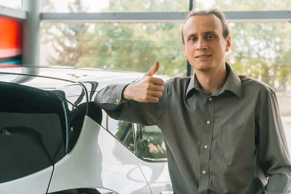 A man in classic clothes stands in a car show on the background of a car. Man bought a new car in the showroom