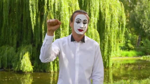 Jeune mime drôle derrière une boîte en verre invisible ou un mur. Mime sur le parc montre pantomime — Video