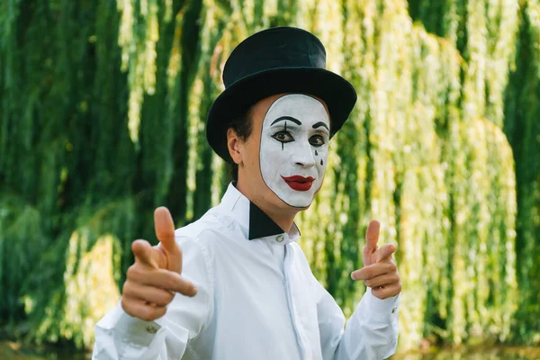 Kameraya bakan bir pandomimcinin yakın çekimi ve parktaki yeşil arka planda gülümsemesi.