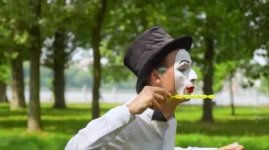 Eğlenceli pandomimci dışarıda sabun köpüğü üflüyor.