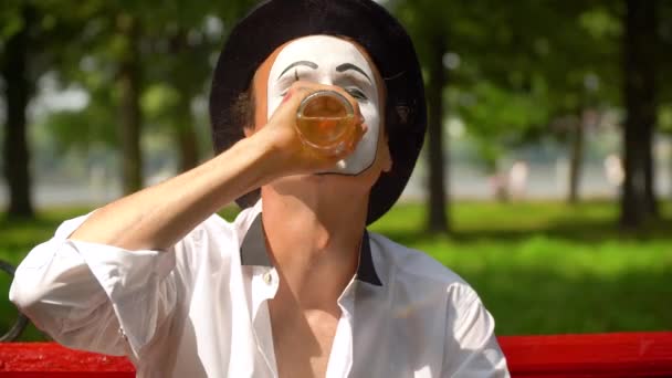 A mímica em um chapéu preto bebe o álcool ao ar livre. Maus hábitos — Vídeo de Stock