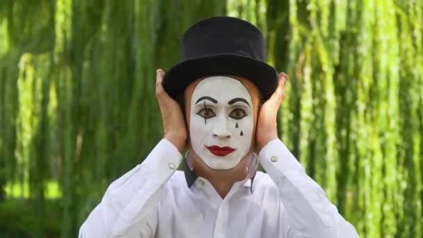 Mima i en svart hatt på parken visar pantomim. Mime stänger öronen, ögonen och munnen med händerna — Stockvideo