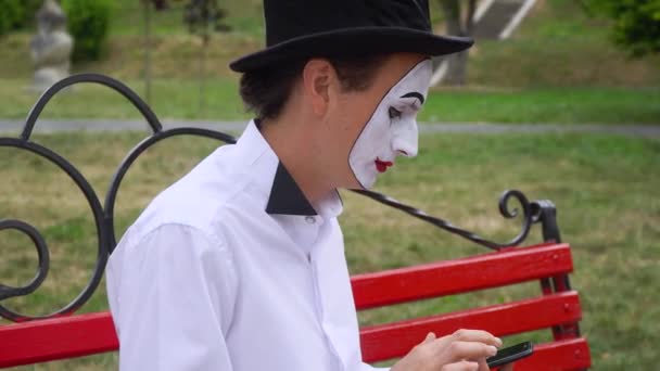 Sjov mime sidder på en park bænk med en telefon – Stock-video