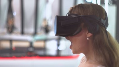 Sanal gerçeklik gözlüğü takan harika bir kız. Arka planda sanal gerçeklik kurulumu. Merak duygusunun ifadesi.