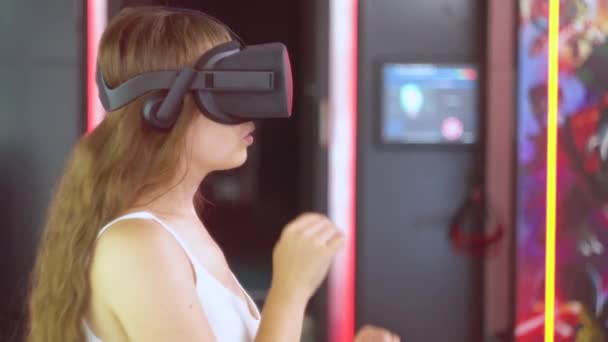 Chica joven en gafas de realidad virtual hace movimientos con las manos como si derribando objetos que se acercan — Vídeo de stock