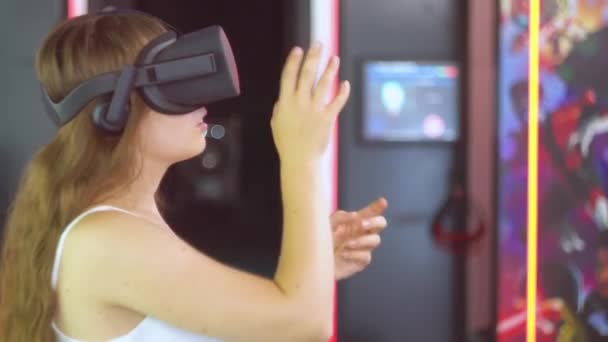 Een jong meisje in virtual reality bril maakt bewegingen met haar handen alsof ze gordijnen opzij trekt — Stockvideo