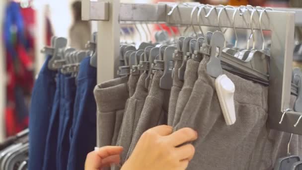 Vrouw kiest broek voor jongen in de winkel. Close-up van de handen — Stockvideo