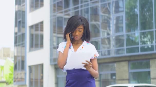 Volwassen Afro-Amerikaanse jonge zakenvrouw praat over de telefoon buiten in de buurt van modern kantoorgebouw — Stockvideo