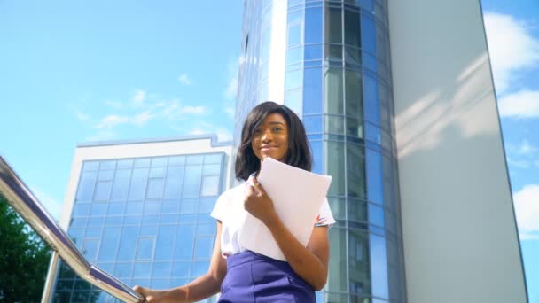 Erwachsene afrikanisch-amerikanische junge Geschäftsfrau arbeitet mit Dokumenten in der Nähe moderner Bürogebäude — Stockvideo