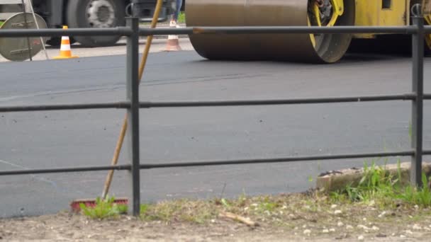Gele road roller rijdt op een weg tijdens het leggen van asfalt. Aanleg van nieuwe weg — Stockvideo