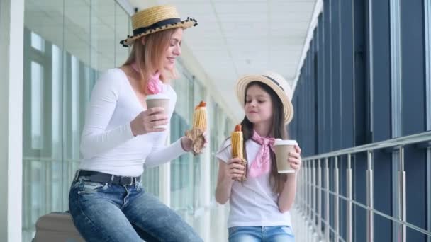 Mãe e filha comem cachorros-quentes e bebem café no aeroporto enquanto esperam pelo avião. Atraso de voo — Vídeo de Stock