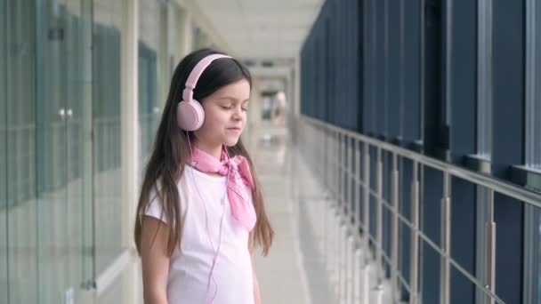 La niña escucha música con auriculares rosas en el aeropuerto. A la espera de vuelo. Fin de la cuarentena — Vídeos de Stock