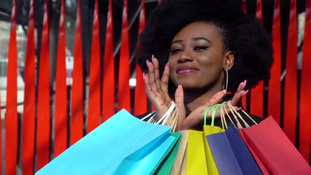 Kırmızı arka planda alışveriş torbaları olan mutlu bir Afrikalı kız. Alışveriş konsepti. Karantinanın sonu — Stok video