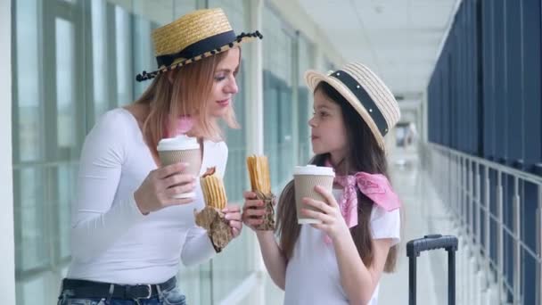 Mulher e menina comem cachorros-quentes e bebem café no aeroporto enquanto esperam pelo avião — Vídeo de Stock