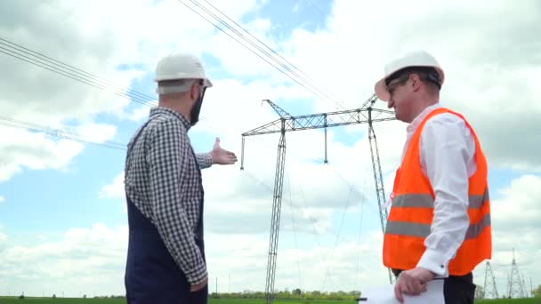 Két mérnök dolgozik a távvezeték közelében. Az igazgató jelentést fogad el az elektromos vezetékek működéséről — Stock videók