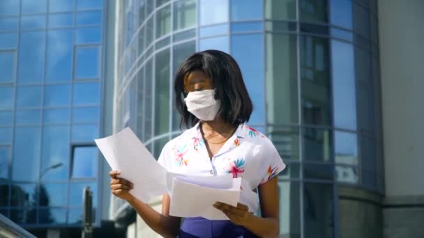 Afroamerikanerin mit Schutzmaske arbeitet in der Nähe eines Geschäftszentrums in einer Metropole mit Dokumenten. Ende der Quarantäne. Covid-19-Schutz — Stockvideo