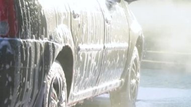 Bir adam makineyi yüksek basınçlı ekipmanla yıkar. Yüksek basınçlı bir su püskürtüsü arabanın kirini temizler. Araba yıkama servisi.