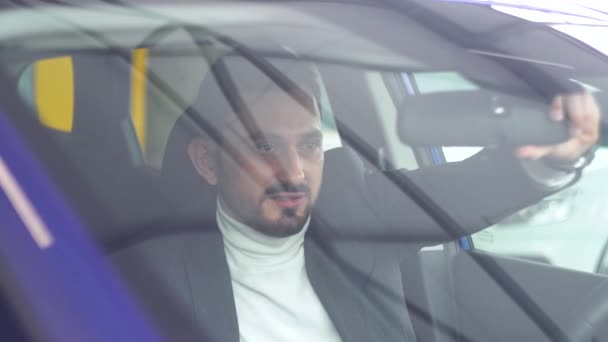 Бородатий чоловік дивиться в дзеркало заднього виду в машині. Вид збоку. Авто бізнес, продаж автомобілів, технології та концепція людей — стокове відео