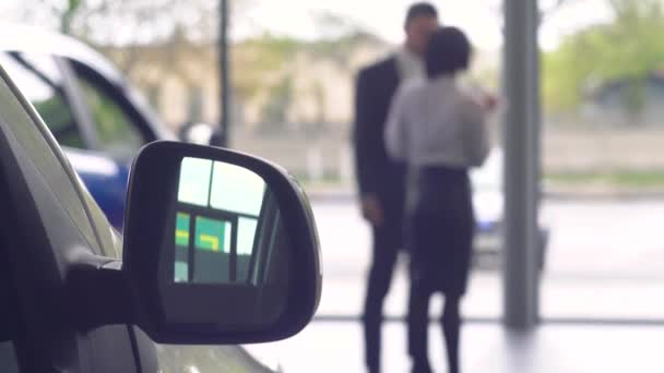 Vista desenfocada del hombre hablando con una concesionaria de autos. Joven chico seguro de sí mismo la elección de automóviles en sala de exposición — Vídeos de Stock