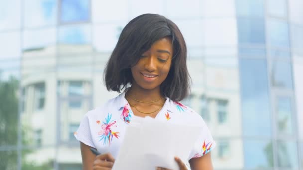 大人のアフリカ系アメリカ人の若いビジネス女性は、近代的なオフィスビルの近くの文書で動作します — ストック動画