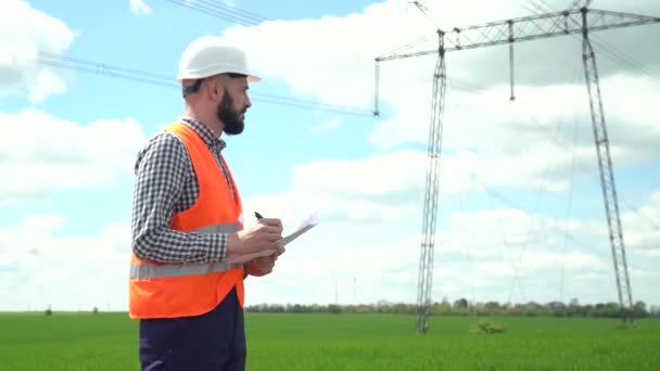 Ingenieur in de buurt van transmissielijnen. Elektrotechnicus controleert hoogspanningsleidingen. Transmissietoren — Stockvideo