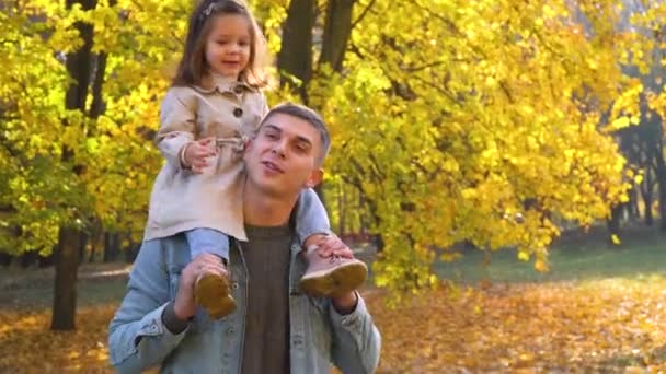 Ojciec bawi się z córką w jesiennym parku. Dziecko na plecach ojca. Szczęśliwa rodzina w jesiennym parku — Wideo stockowe