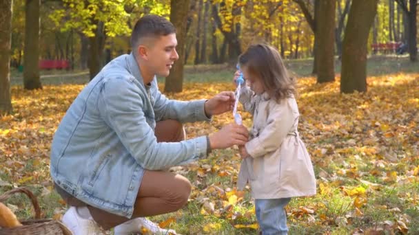 Apa légbuborékokat fúj a kislányával az őszi parkban. — Stock videók