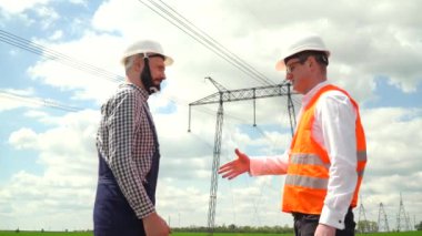 İletişim hatları yakınında çalışan iki mühendis. Enerji işbirliği. Aktarım kuleleri