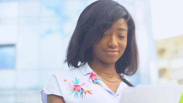 大人のアフリカ系アメリカ人の若いビジネス女性は、近代的なオフィスビルの近くの文書で動作します。検疫終了 — ストック動画