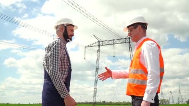 Twee ingenieurs in de buurt van transmissielijnen. Samenwerking op energiegebied. Transmissietoren — Stockvideo