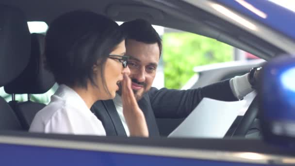 Şık bir adam araba kuaföründe oturmuş kadın araba satıcısıyla konuşuyor. Galeride otomobil seçen kendine güvenen genç adam. — Stok video