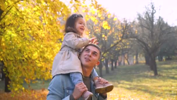 Pai brincando com sua filhinha no parque de outono. Criança nas costas do pai. Família feliz no parque de outono — Vídeo de Stock